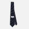 View 4 of product The Turnbull & Asser Navy Zigzag Jacquard Silk Tie is crafted from fine English silk, featuring a navy base with thin white zigzag stripes and shown rolled up on a plain white background.