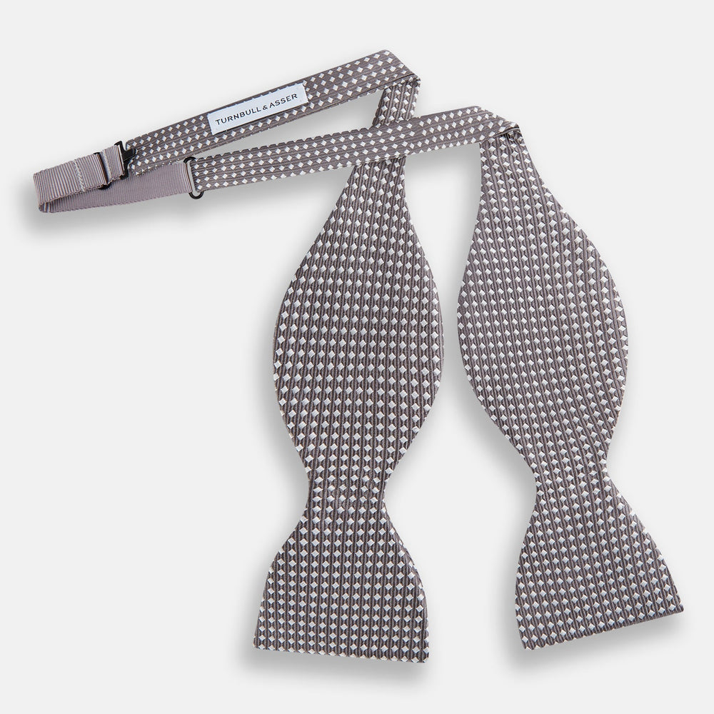 The Turnbull & Asser Grey and White Diamond Silk Bow Tie showcases a subtle diamond pattern, ideal for formalwear, and is elegantly displayed against a plain white background.
