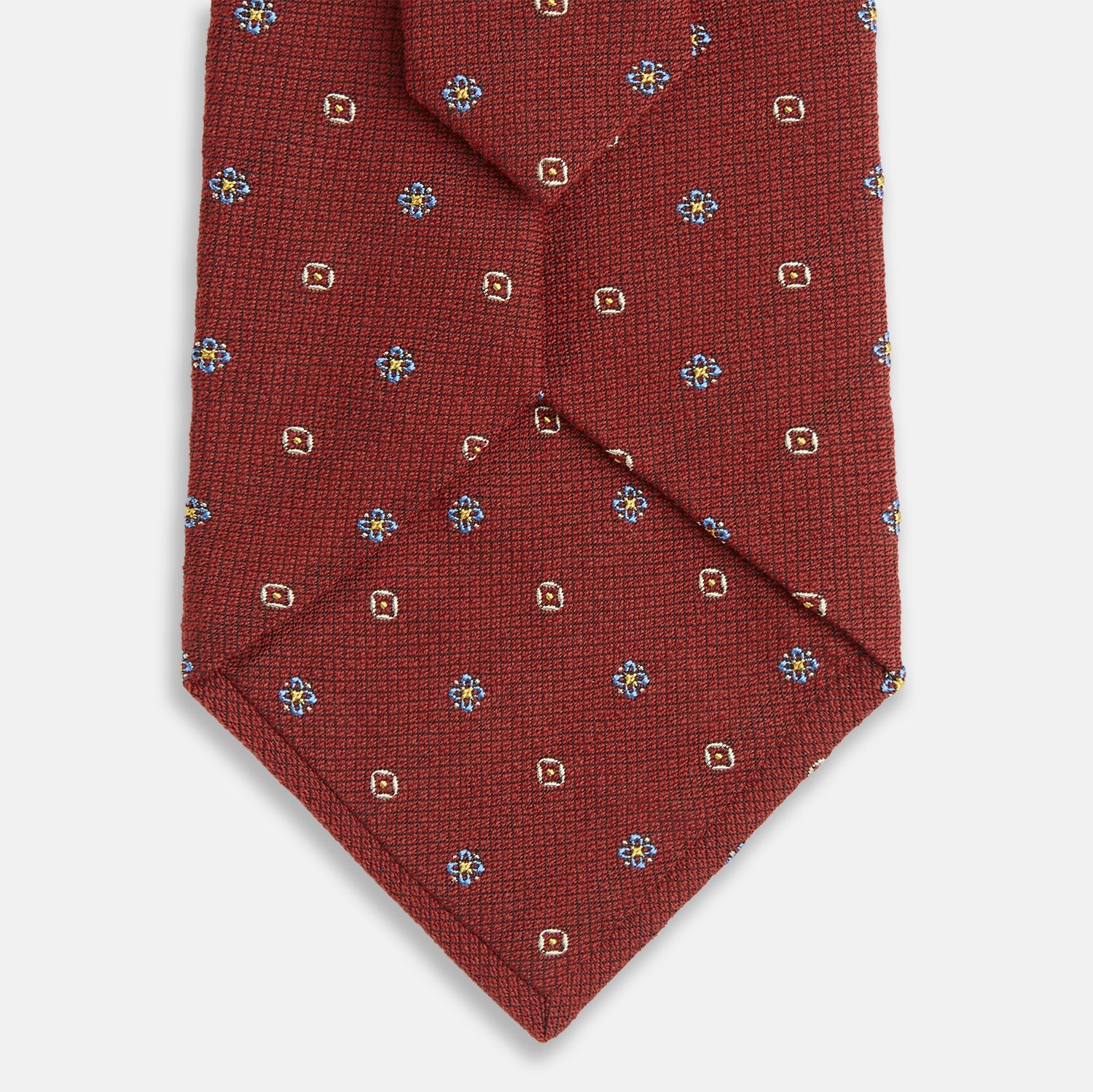 View 3 of product A Turnbull & Asser Red Motif Silk Tie featuring small blue and yellow floral designs with brown geometric shapes is displayed rolled up on a plain white background.