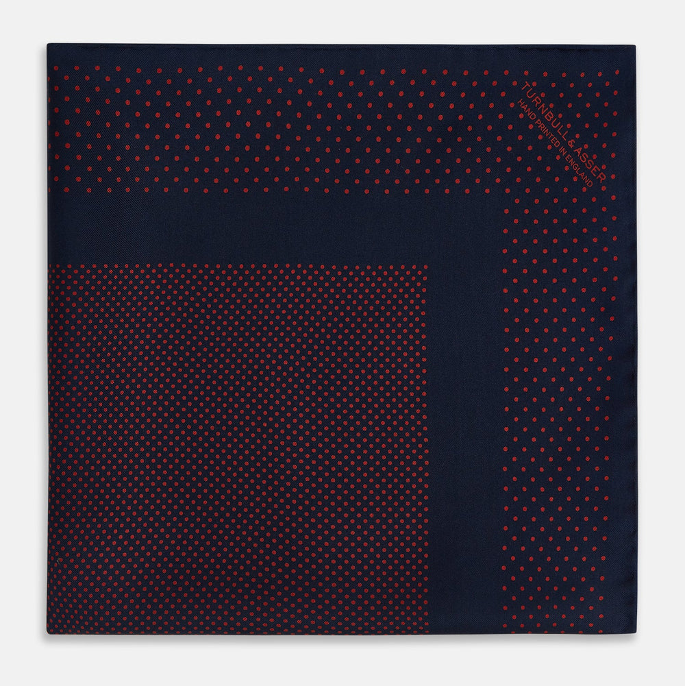 The Turnbull & Asser Navy and Red Dot Silk Pocket Square features a dark navy blue base with small red polka dots on the border and inner pattern, all handmade and neatly folded.