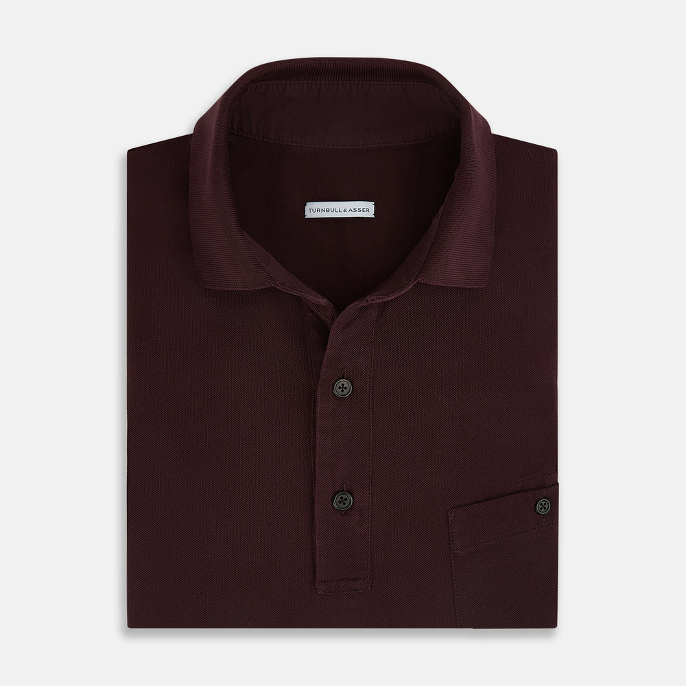 The Turnbull & Asser Burgundy Polo Shirt is crafted from soft cotton jersey with short sleeves, a classic collar, three front buttons, and a small buttoned chest pocket, shown flat on a white background.