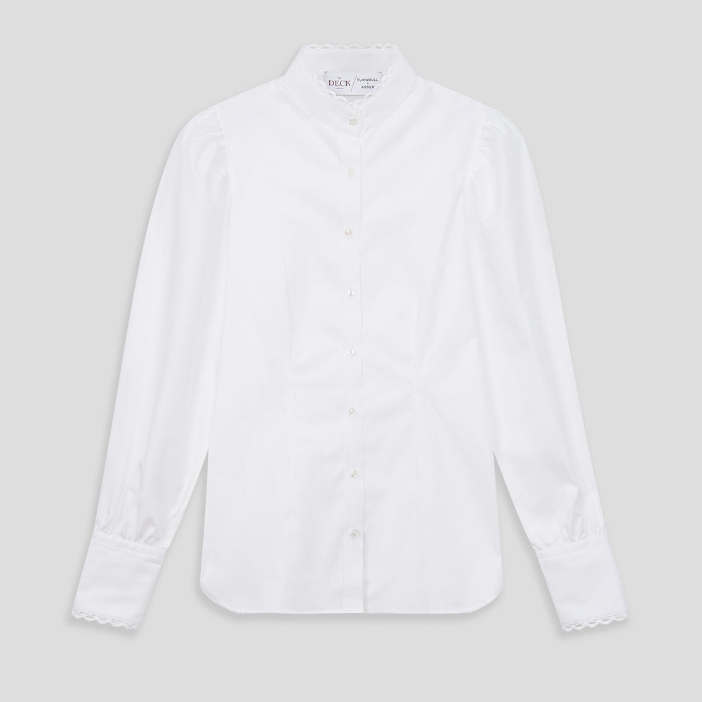A woman stands in profile, looking down with hands in her pockets, wearing the Turnbull & Asser Turnbull and The Deck White Cotton Expressionist Shirt, paired with high-waisted black-and-white houndstooth pants.