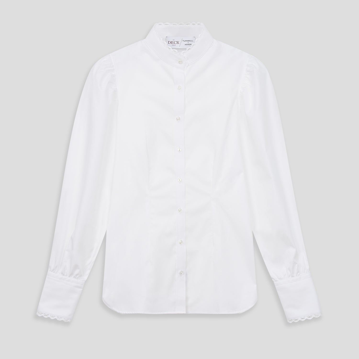 View 2 of product A woman stands in profile, looking down with hands in her pockets, wearing the Turnbull & Asser Turnbull and The Deck White Cotton Expressionist Shirt, paired with high-waisted black-and-white houndstooth pants.