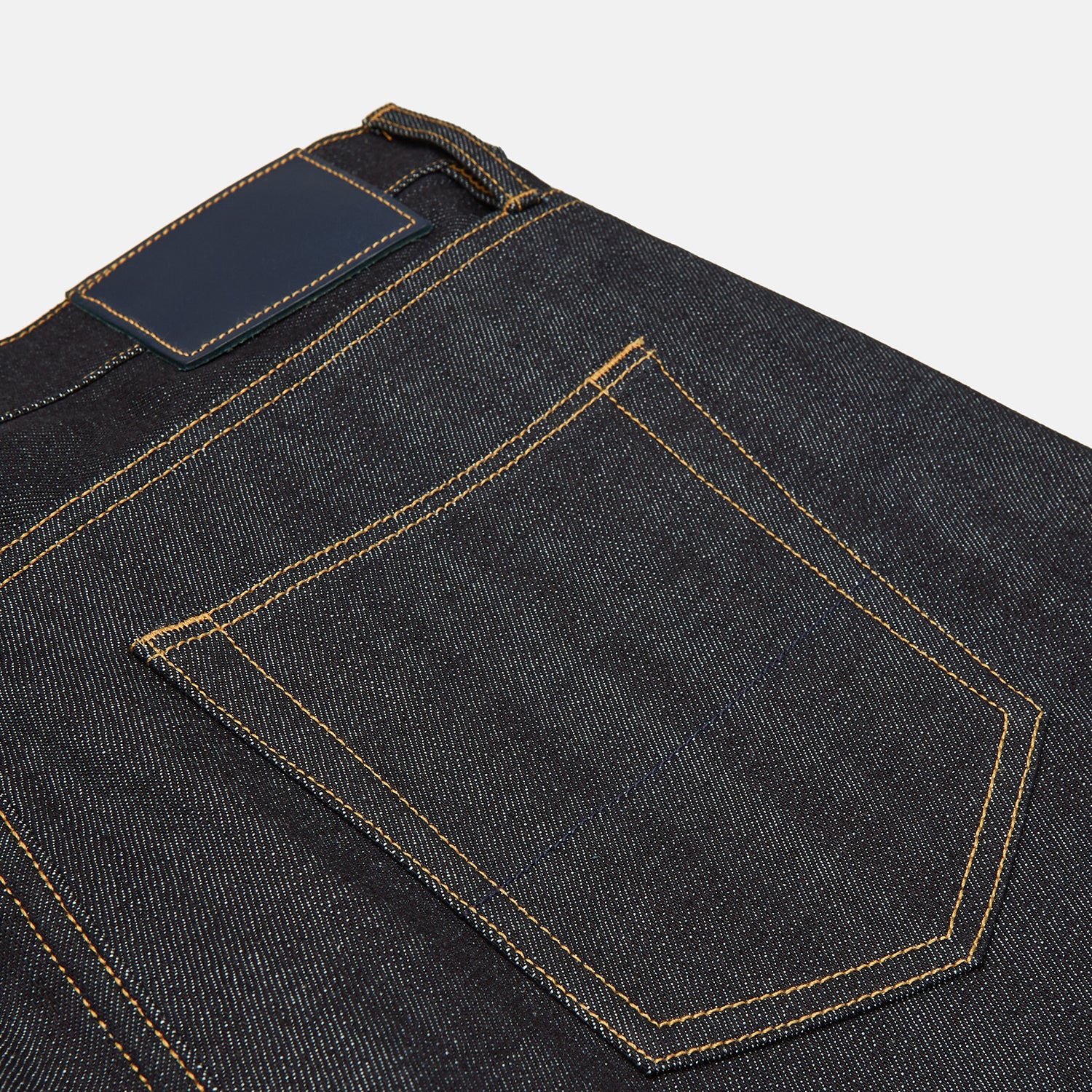 View 3 of product A pair of Turnbull & Asser Indigo Japanese Selvedge Denim Jeans in dark blue with rolled-up cuffs, yellow stitching, five pockets, and a button fly, laid flat on a white background.
