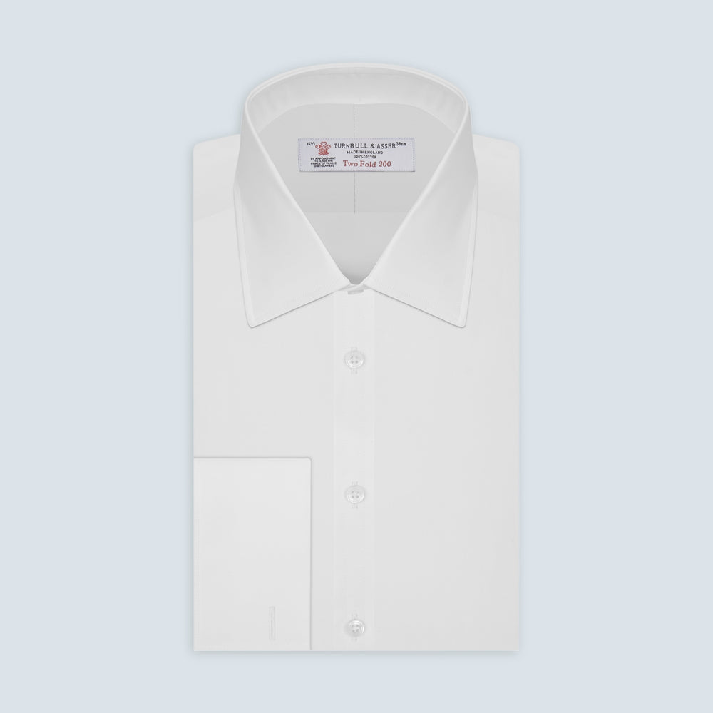 A Turnbull & Asser Two-Fold 200 White Cotton Shirt with T&A collar and double cuffs, neatly folded to show the label inside the collar, is displayed on a light blue background.
