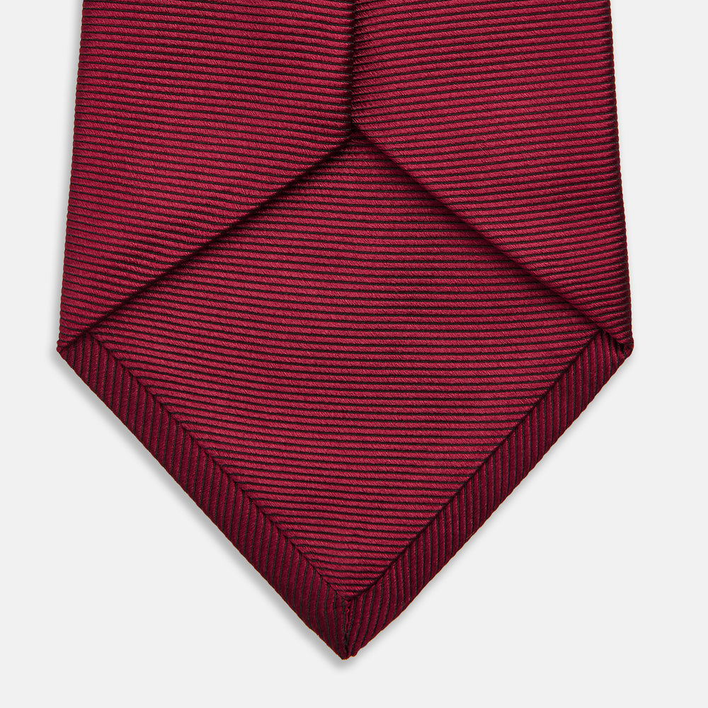 A close-up of the Turnbull & Asser HORIZONTAL TWILL BURGUNDY TIE, a textured men's accessory, rolled up and displayed on a plain white background.