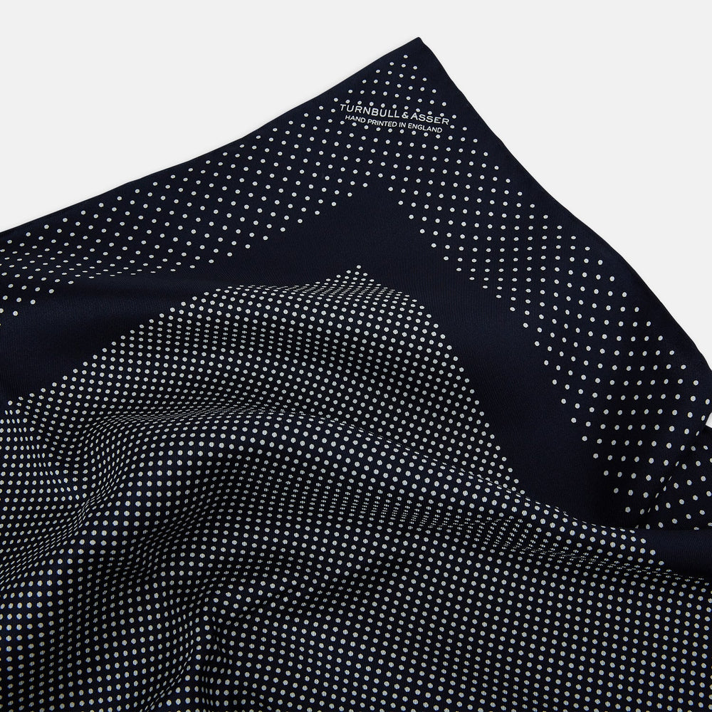 The Turnbull & Asser Navy and White Dot Silk Pocket Square features evenly spaced white polka dots on navy, a solid navy border, and one folded corner to reveal the reverse side, highlighting its fine handmade craftsmanship.