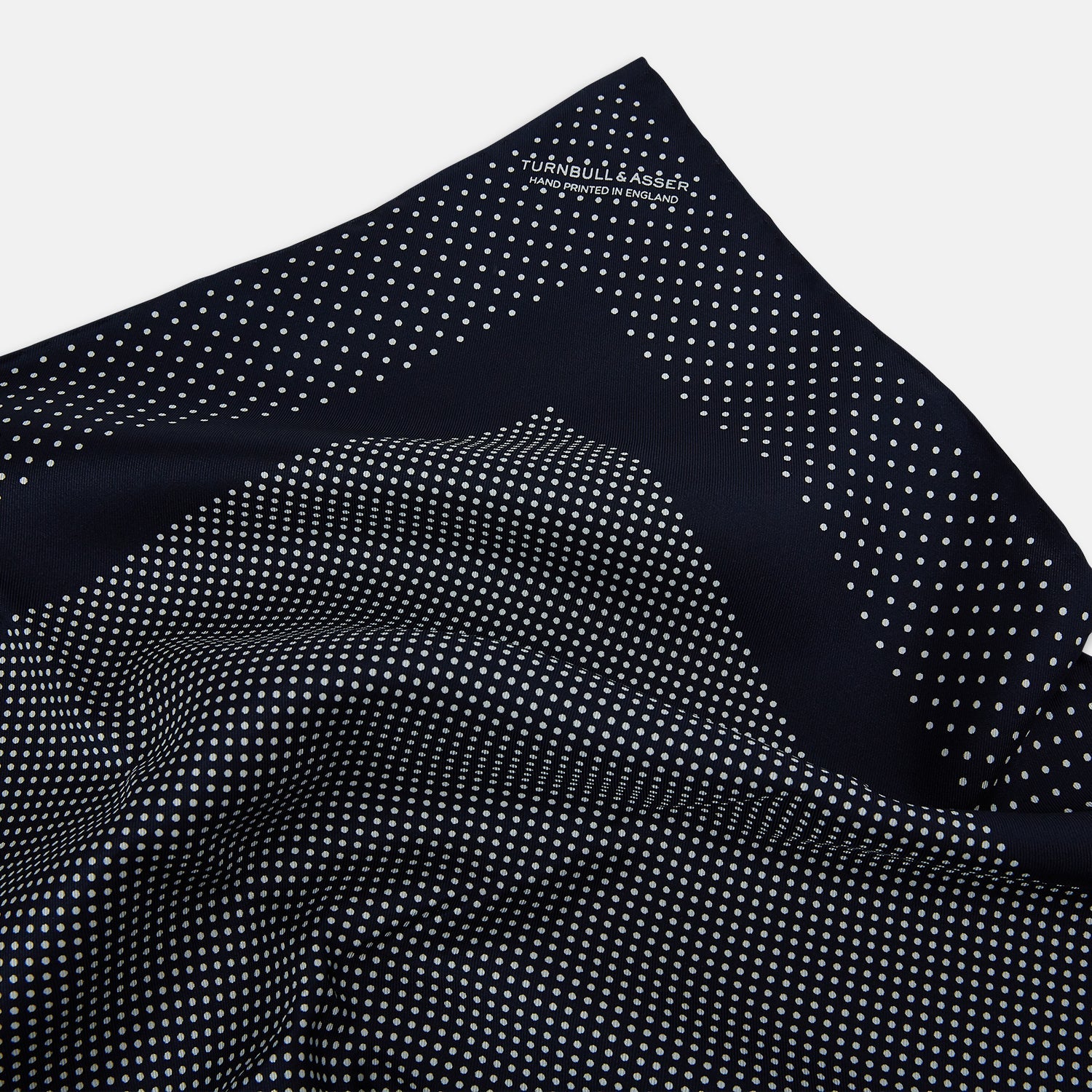 View 2 of product The Turnbull & Asser Navy and White Dot Silk Pocket Square features evenly spaced white polka dots on navy, a solid navy border, and one folded corner to reveal the reverse side, highlighting its fine handmade craftsmanship.