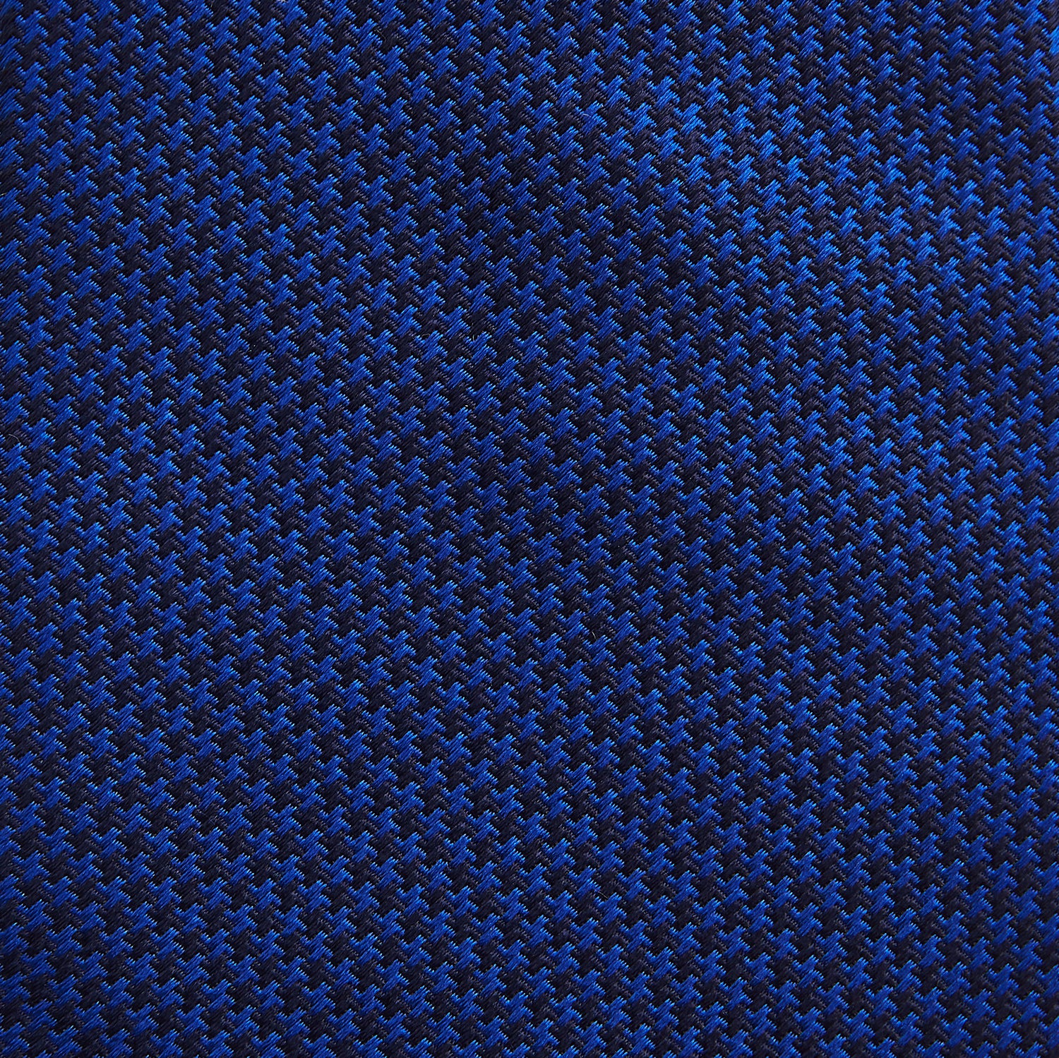 View 3 of product The HOUNDSTOOTH NAVY CRUISE TIE by Turnbull & Asser, featuring a textured blue design, is displayed rolled-up on a plain white background—an essential accessory for elevating formal looks.