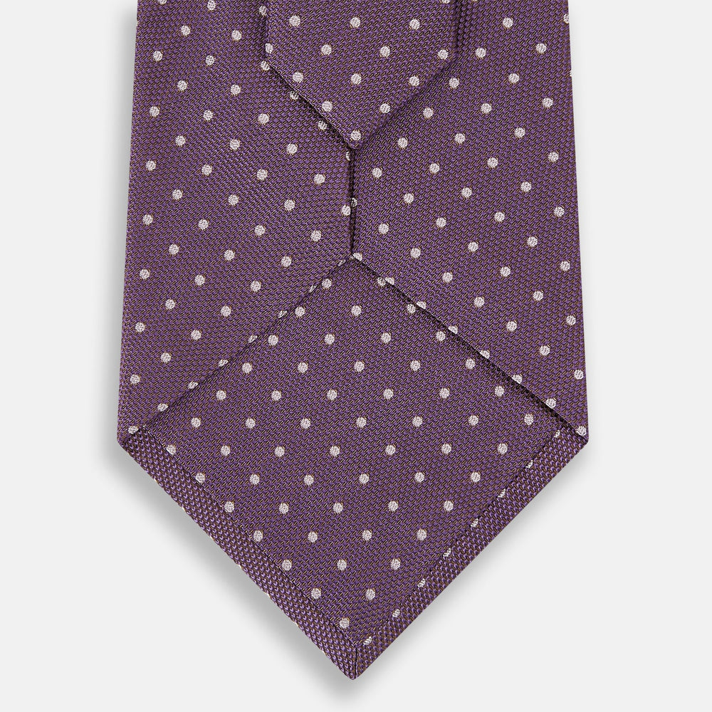 The Turnbull & Asser Lilac and Purple Micro Dot Silk Tie, featuring small white dots, is a stylish accessory for smart attire. Displayed rolled-up on a light background.