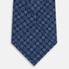 View 3 of product The Turnbull & Asser Dark Navy Floral Tile Pattern Printed Silk Tie, rolled up and displayed on a white background, features a blue geometric and floral pattern.