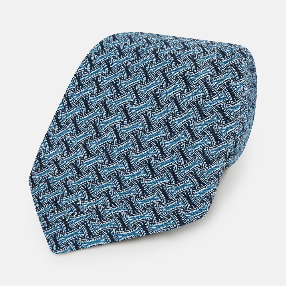 A close-up of the Turnbull & Asser Pale Blue and Navy Weave Patterned Silk Tie, featuring a textured geometric design. The silk tie is rolled at one end and displayed on a white background.