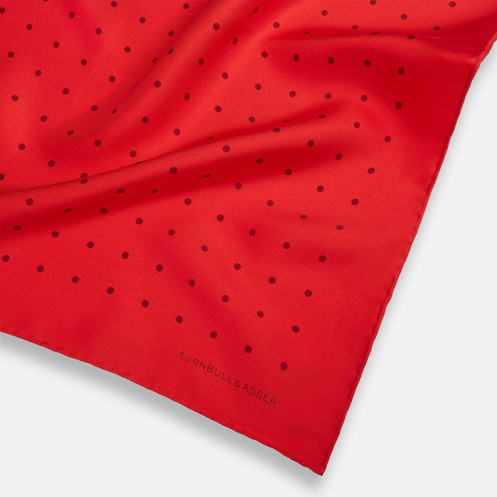 The Turnbull & Asser Red and Burgundy Spot Silk Pocket Square features evenly spaced small spots and the brand logo in the bottom right corner—perfect for formal wear. One corner is folded to show the reverse side.