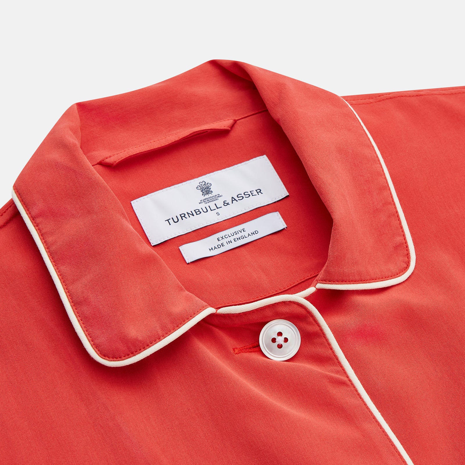 View 4 of product The Turnbull & Asser Women's Coral Pink Silk Thelma Pyjama Set features a long-sleeve button-up top with two front pockets and matching drawstring pants, shown on a white background.