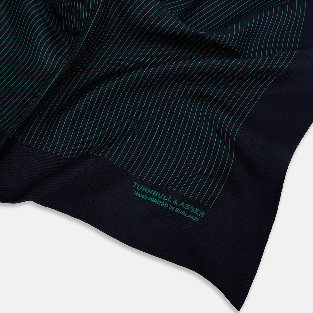 The Turnbull & Asser Navy and Hunter Green Stripe Silk Pocket Square features thin green stripes, hand-rolled edges, and "TURNBULL & ASSER HAND PRINTED IN ENGLAND" in green on the bottom right corner.