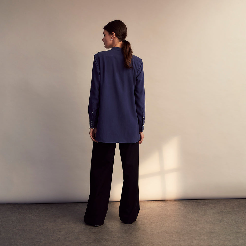 The Turnbull & Asser Blue Soft-touch Silk Lauren Shirt is a navy, long-sleeve button-up with an Igret stand collar, white buttons, curved hem, relaxed fit, and elongated body for a modern look, shown laid flat on a white background.