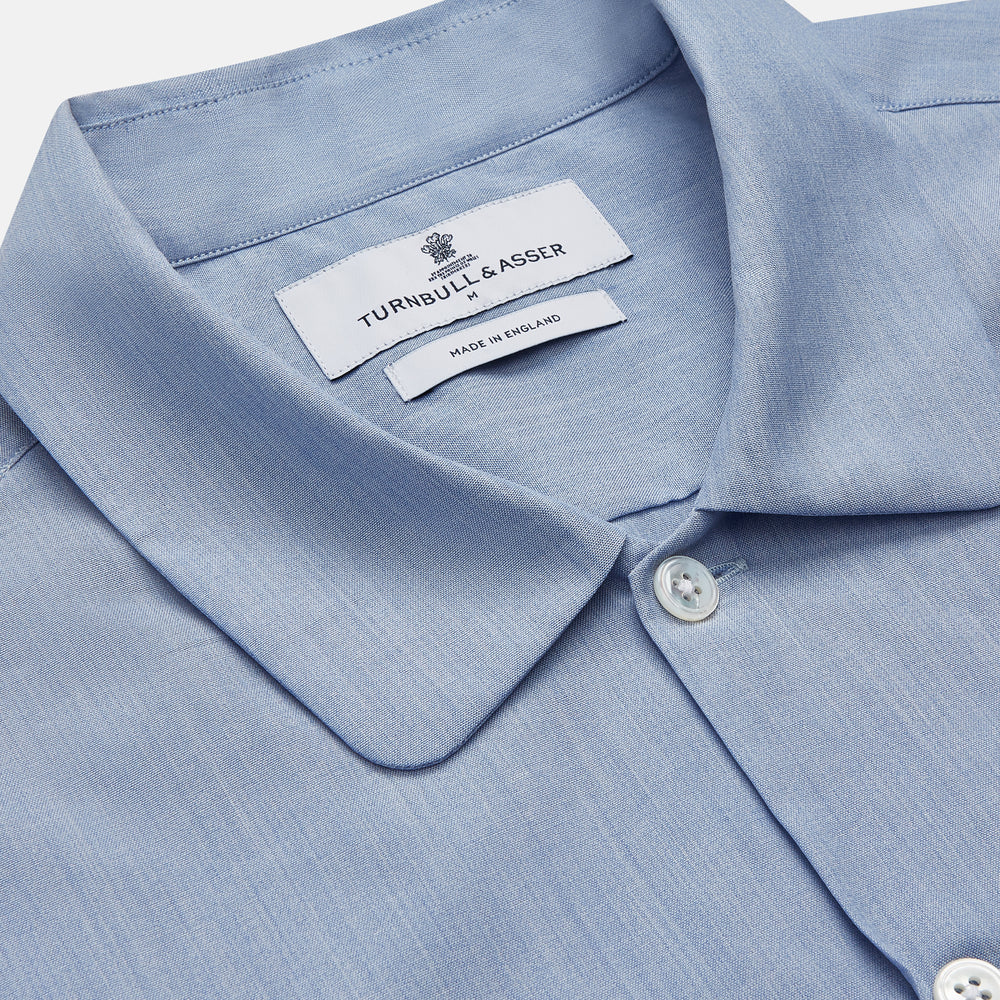 The Turnbull & Asser Slate Blue Chambray Holiday Fit Fellows Shirt features long sleeves and a classic collar, laid flat on a white background—a versatile summer piece for any occasion.