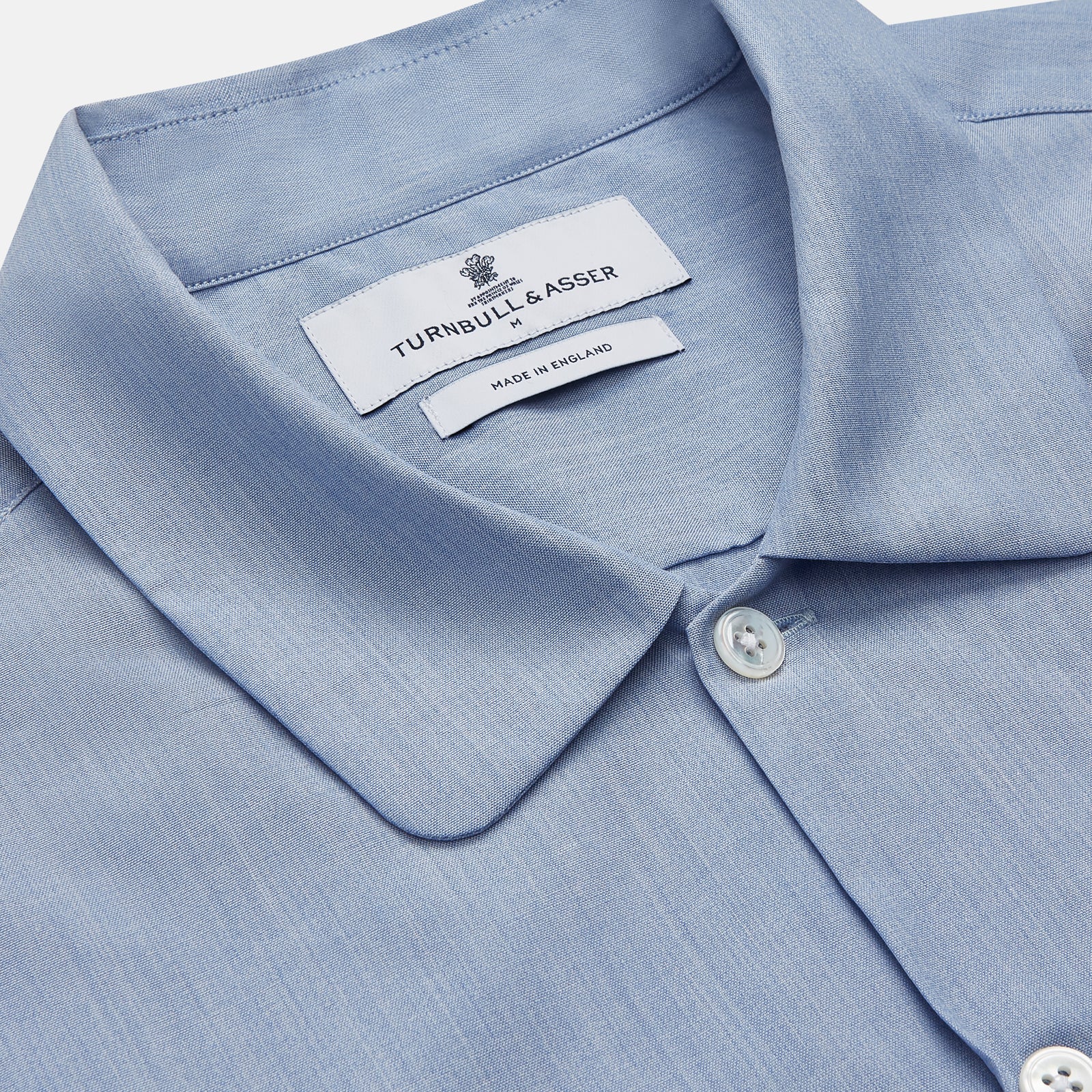 View 3 of product The Turnbull & Asser Slate Blue Chambray Holiday Fit Fellows Shirt features long sleeves and a classic collar, laid flat on a white background—a versatile summer piece for any occasion.