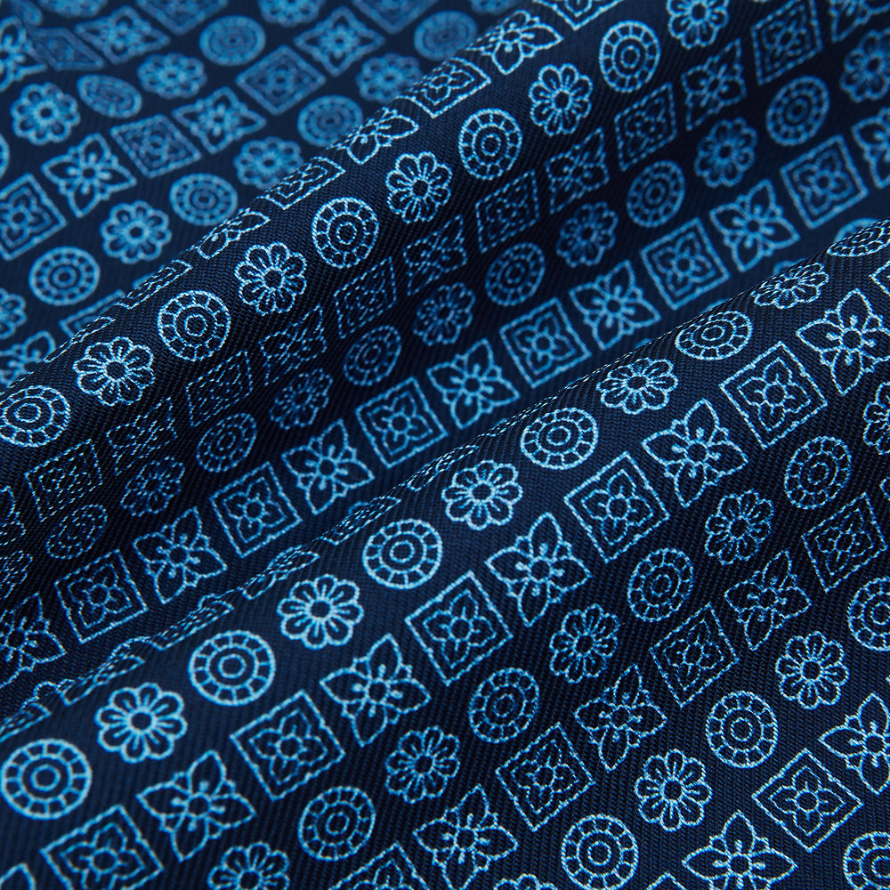The Turnbull & Asser Dark Navy Floral Tile Pattern Printed Silk Cravat features a British-inspired light blue floral tile design, elegantly displayed on a white background.