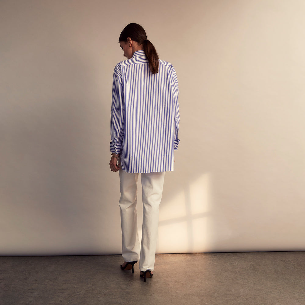 The Turnbull & Asser Pale Blue Candy Stripe Cotton Marlene Shirt is an oversized women's collared shirt with long sleeves, buttoned cuffs, and vertical blue and white stripes, shown laid flat on a white background.