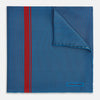 View 1 of product A blue silk pocket square by Turnbull & Asser, featuring thin black stripes, a striking vertical red stripe, and a turned-over corner that reveals the reverse side. The brand name is printed discreetly in one corner.
