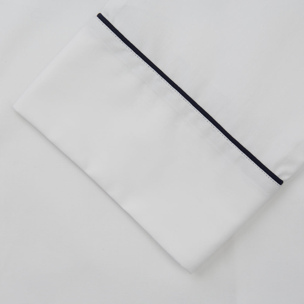 The Turnbull & Asser Women's Harriet Plain White Cotton Pyjama Set features long sleeves, black piping, a chest pocket, and matching pants with elastic waistband and ribbon tie, all displayed on a white background.
