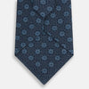 View 3 of product The Turnbull & Asser Navy Medallion Silk Tie is crafted from fine English silk, featuring light blue geometric medallions on a white background, and is rolled neatly with the pointed end facing forward.
