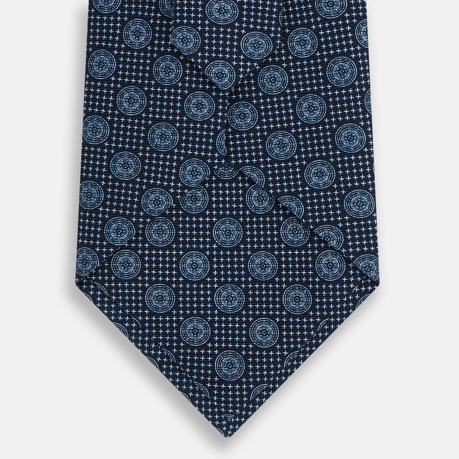 View 3 of product The Turnbull & Asser Navy Medallion Silk Tie is crafted from fine English silk, featuring light blue geometric medallions on a white background, and is rolled neatly with the pointed end facing forward.