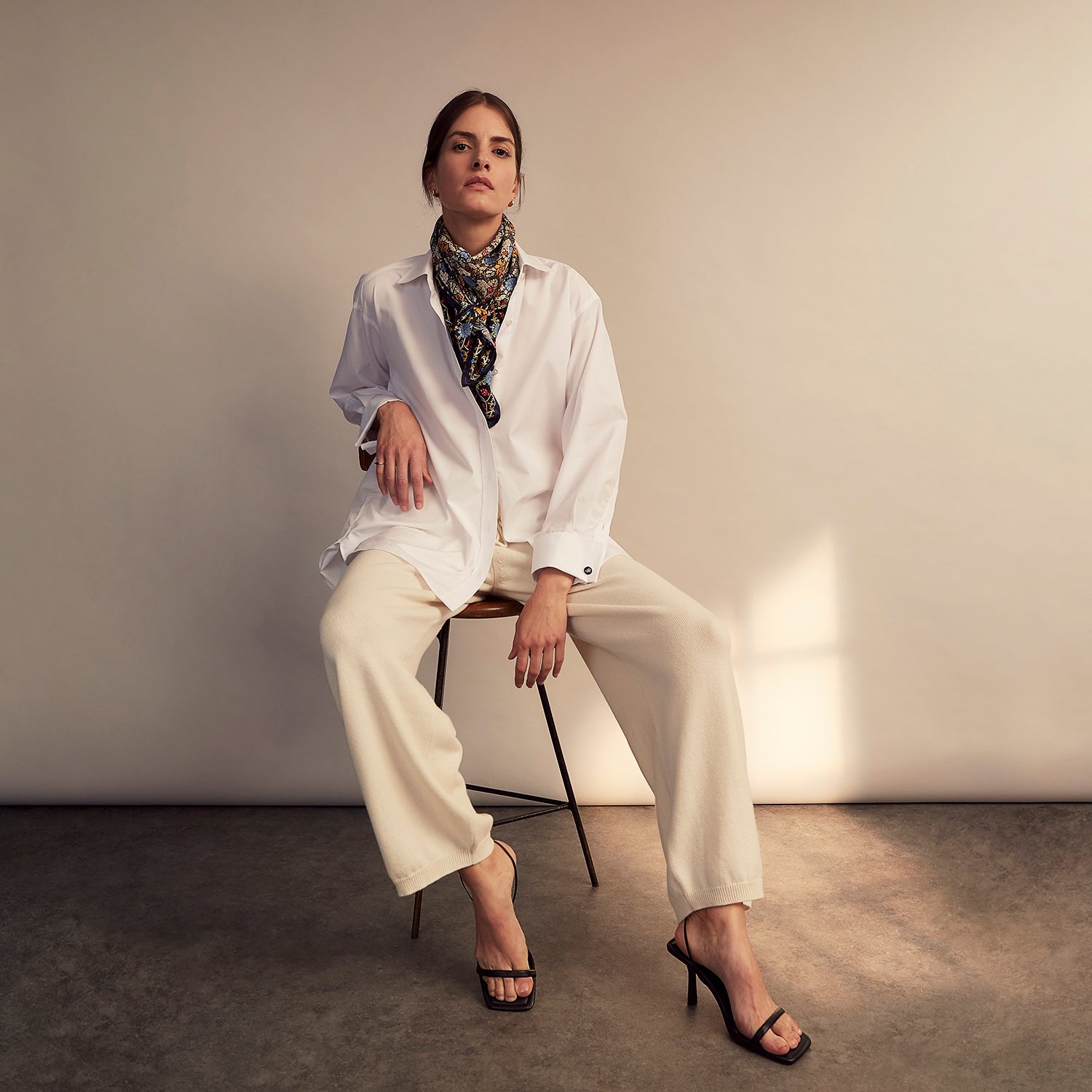 View 7 of product A woman with straight brown hair pulled back wears the Turnbull & Asser White Cotton Marlene Shirt, featuring classic menswear details, paired with high-waisted cream trousers against a neutral background.