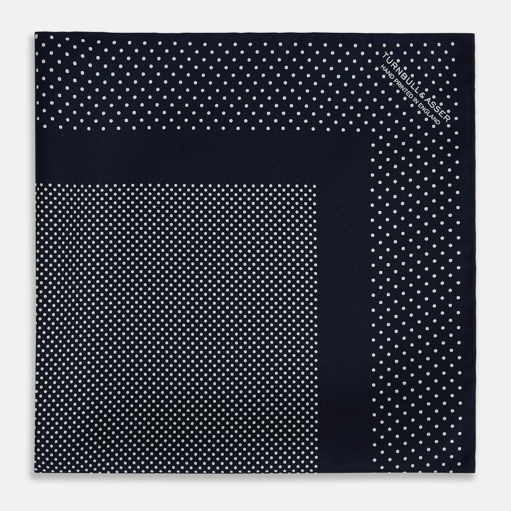The Turnbull & Asser Navy and White Dot Silk Pocket Square features evenly spaced white polka dots on navy, a solid navy border, and one folded corner to reveal the reverse side, highlighting its fine handmade craftsmanship.