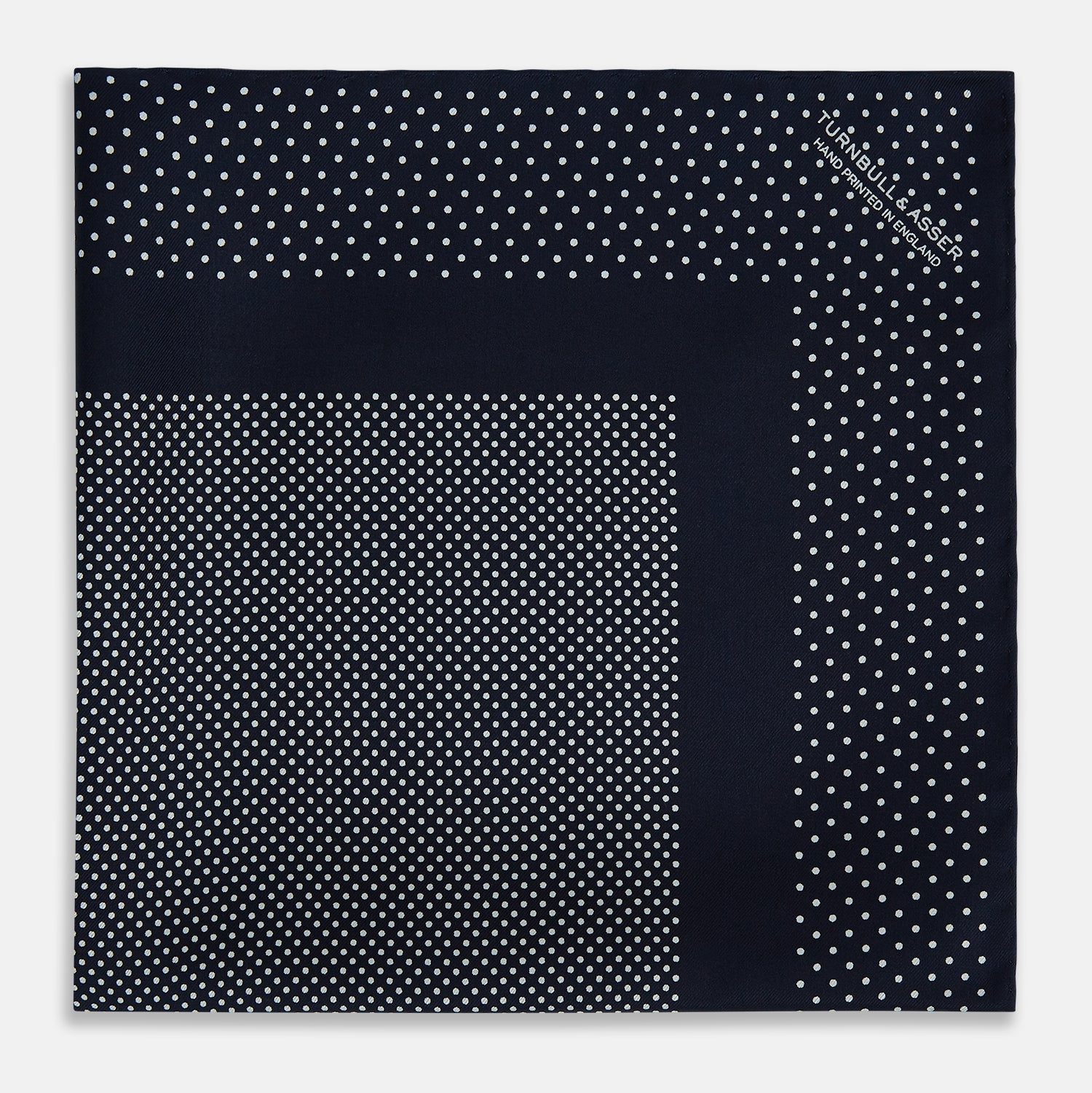 View 3 of product The Turnbull & Asser Navy and White Dot Silk Pocket Square features evenly spaced white polka dots on navy, a solid navy border, and one folded corner to reveal the reverse side, highlighting its fine handmade craftsmanship.