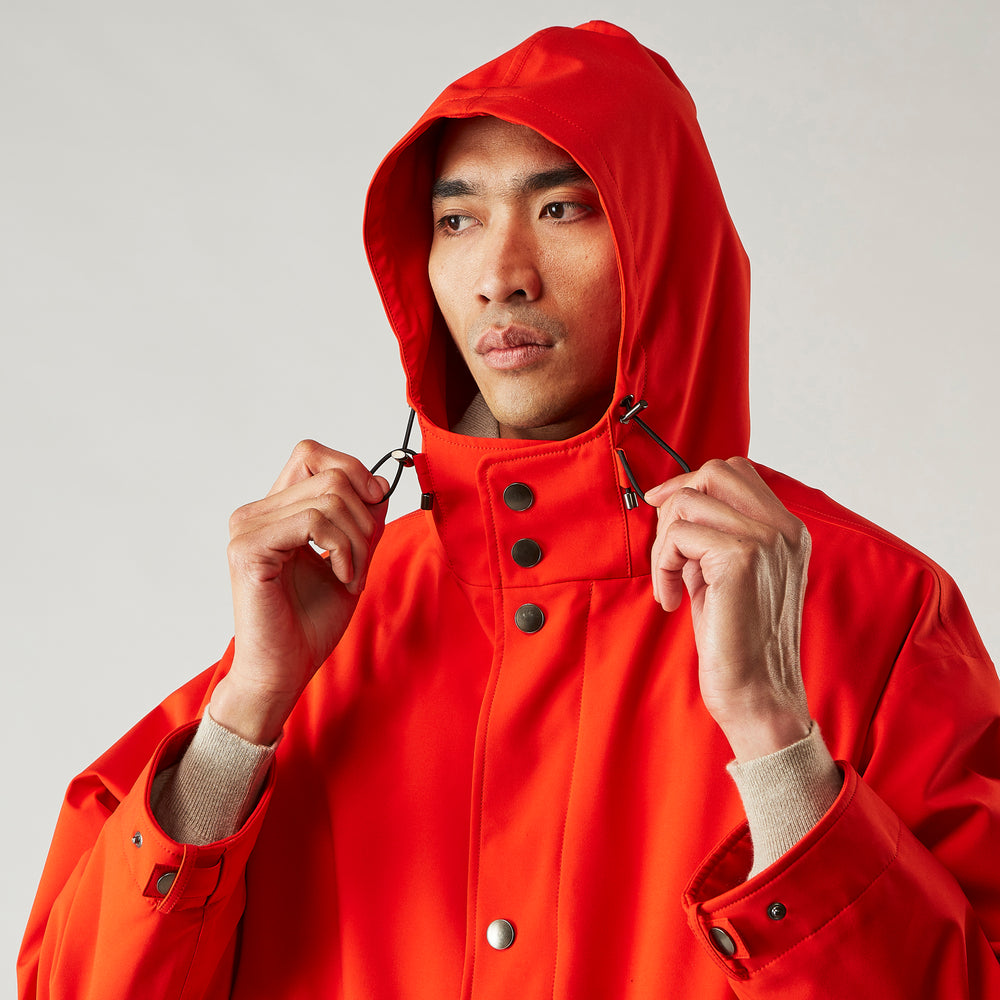 Wearing the Turnbull & Asser Red Walter Sealup Parka with Detachable Liner, black pants, and white sneakers, a person stands in profile against a plain light background—perfect for travel.
