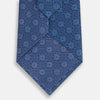 View 3 of product The Turnbull & Asser Azzurro Medallion Silk Tie, rolled up and displayed on a white background, features small geometric medallion motifs in lighter blue tones.