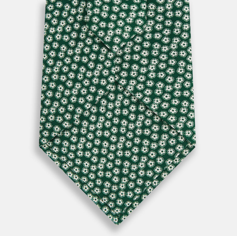 The Forest Green Flower Patterned Silk Tie by Turnbull & Asser features a white floral motif on silk, shown neatly rolled against a plain white background.