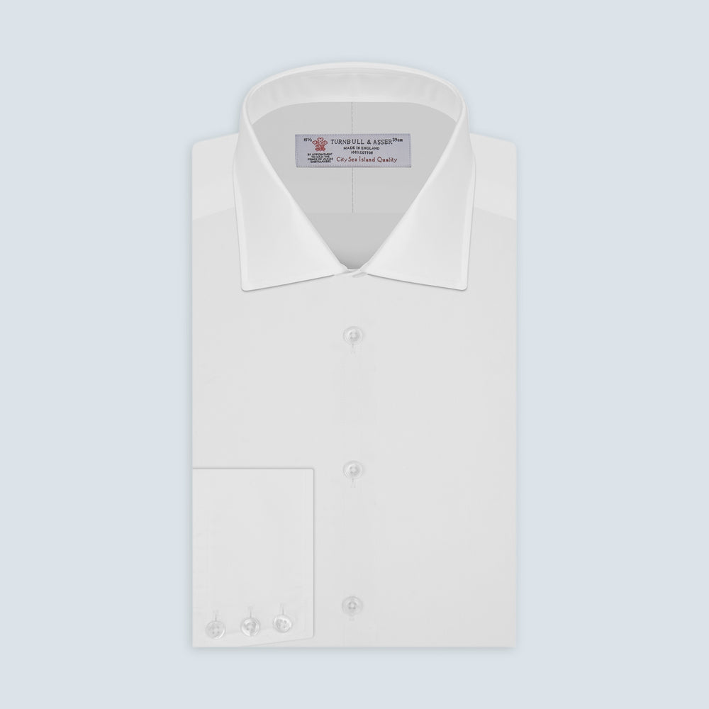 The Sea Island Cotton Classic Fit White Shirt by Turnbull & Asser features a classic collar and front buttons, neatly folded with its label visible, displayed on a light blue background.