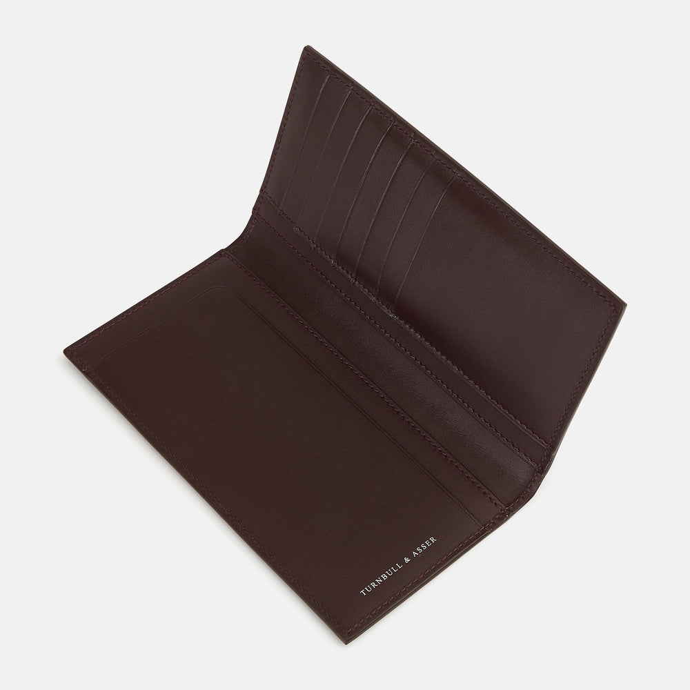 The Turnbull & Asser Burgundy B Cut Continental Wallet, with smooth, unadorned surfaces and visible edge stitching, is pictured closed in rich burgundy Italian leather against a white background.