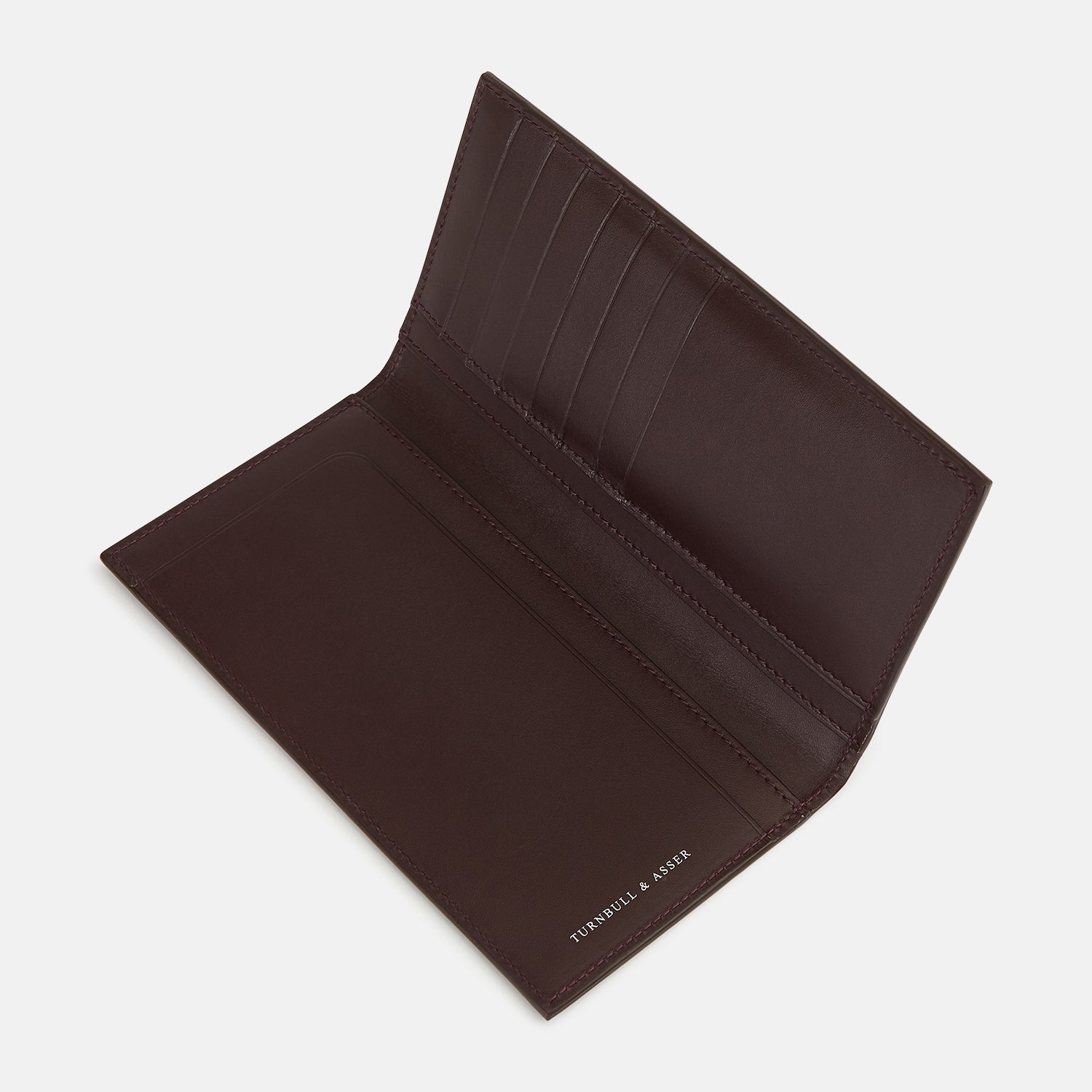 View 3 of product The Turnbull & Asser Burgundy B Cut Continental Wallet, with smooth, unadorned surfaces and visible edge stitching, is pictured closed in rich burgundy Italian leather against a white background.