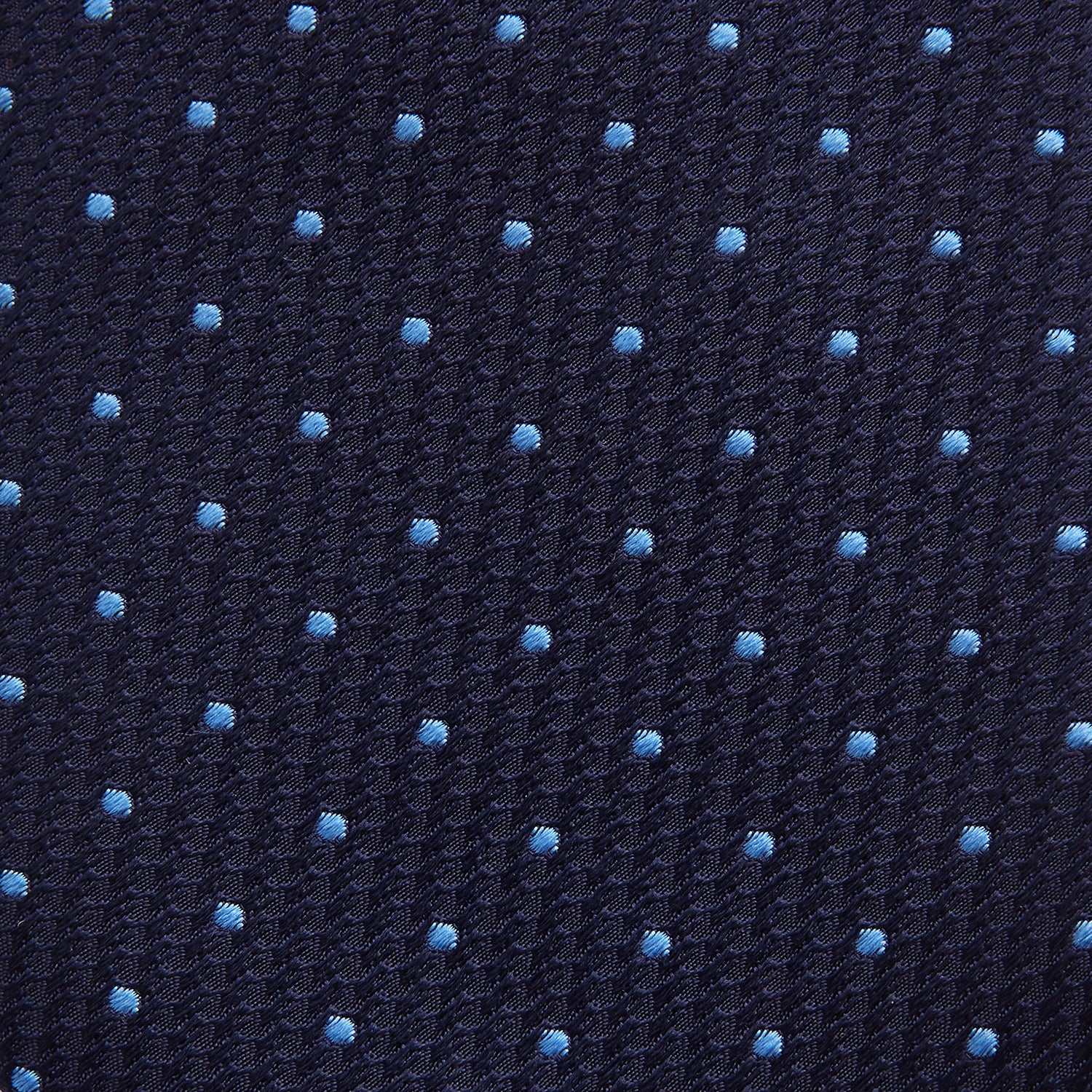 View 3 of product The LACE ON TONE SPOT NAVY FORD TIE by Turnbull & Asser is a rolled-up navy tie with textured fabric and an evenly spaced pattern of small light blue polka dots.