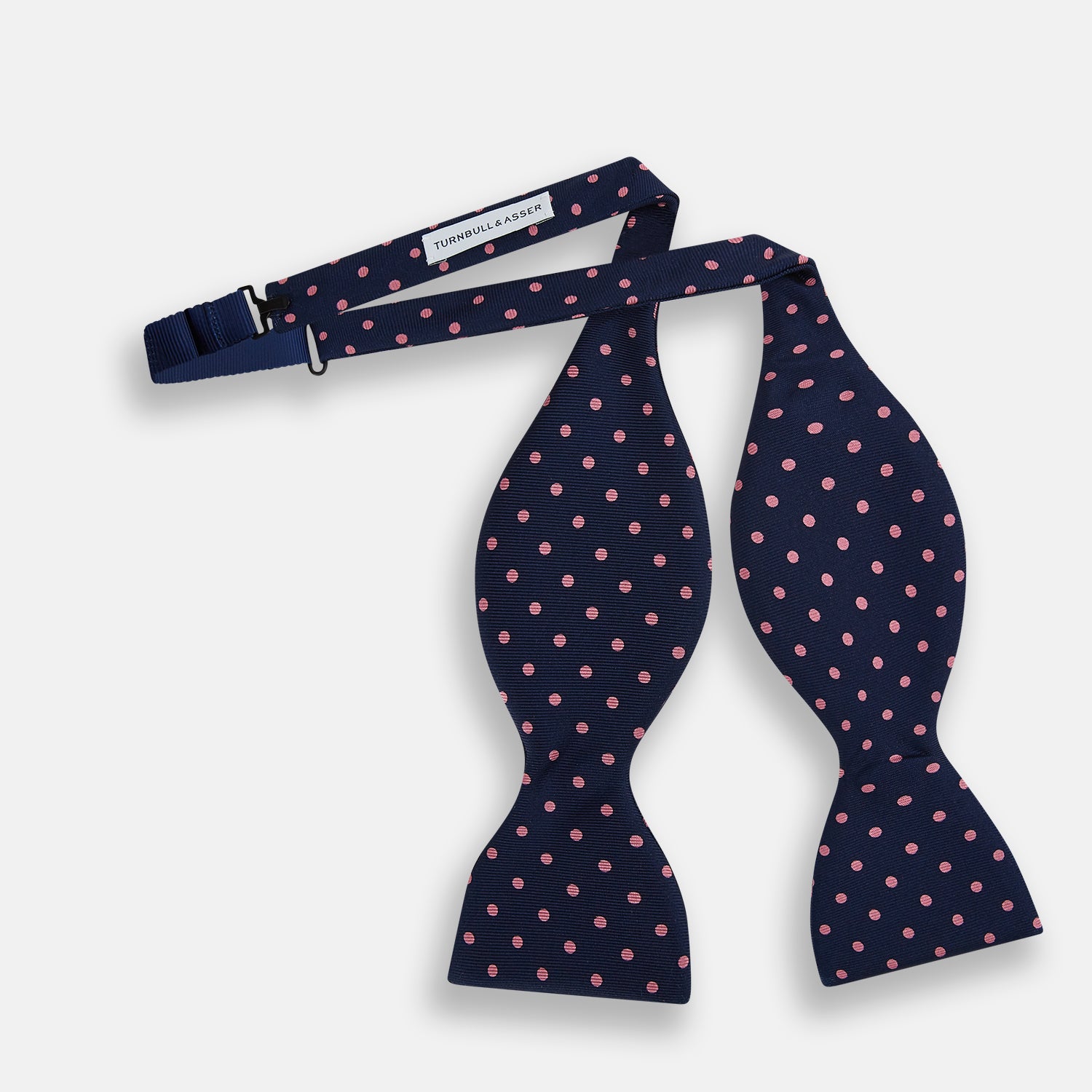 View 2 of product The Navy and Pink Spot Silk Bow Tie by Turnbull & Asser features evenly spaced pink polka dots on navy silk, shown against a plain white background.