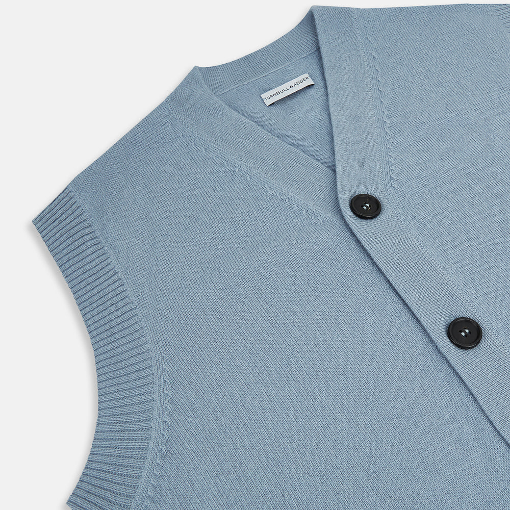 The Turnbull & Asser Frost Blue Cashmere Sleeveless Cardigan features a V-neck, five black buttons, two front pockets, and ribbed trim—ideal for layering in sophisticated outfits.