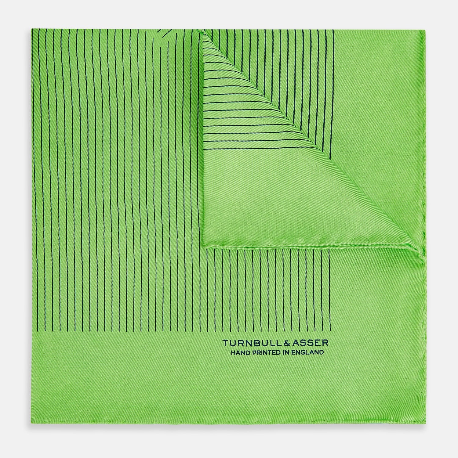 View 1 of product The Fern Green Stripe Silk Pocket Square by Turnbull & Asser features thin black vertical stripes, celebrates British heritage, and is inscribed “TURNBULL & ASSER HAND PRINTED IN ENGLAND” in one corner; one corner is folded inward.