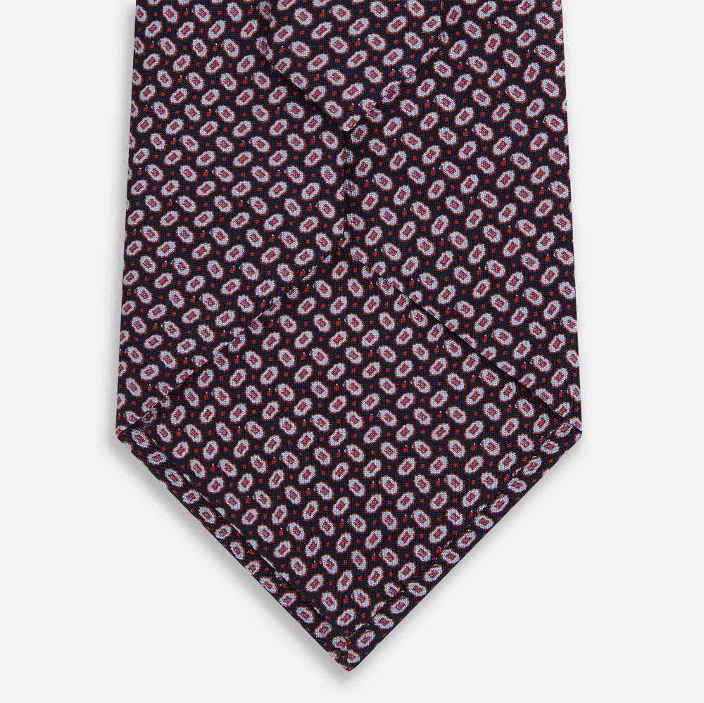 The Turnbull & Asser Red and Navy Oval-Patterned Silk Tie features a refined oval motif on navy silk, ideal for formal wear, and is showcased on a plain white background.