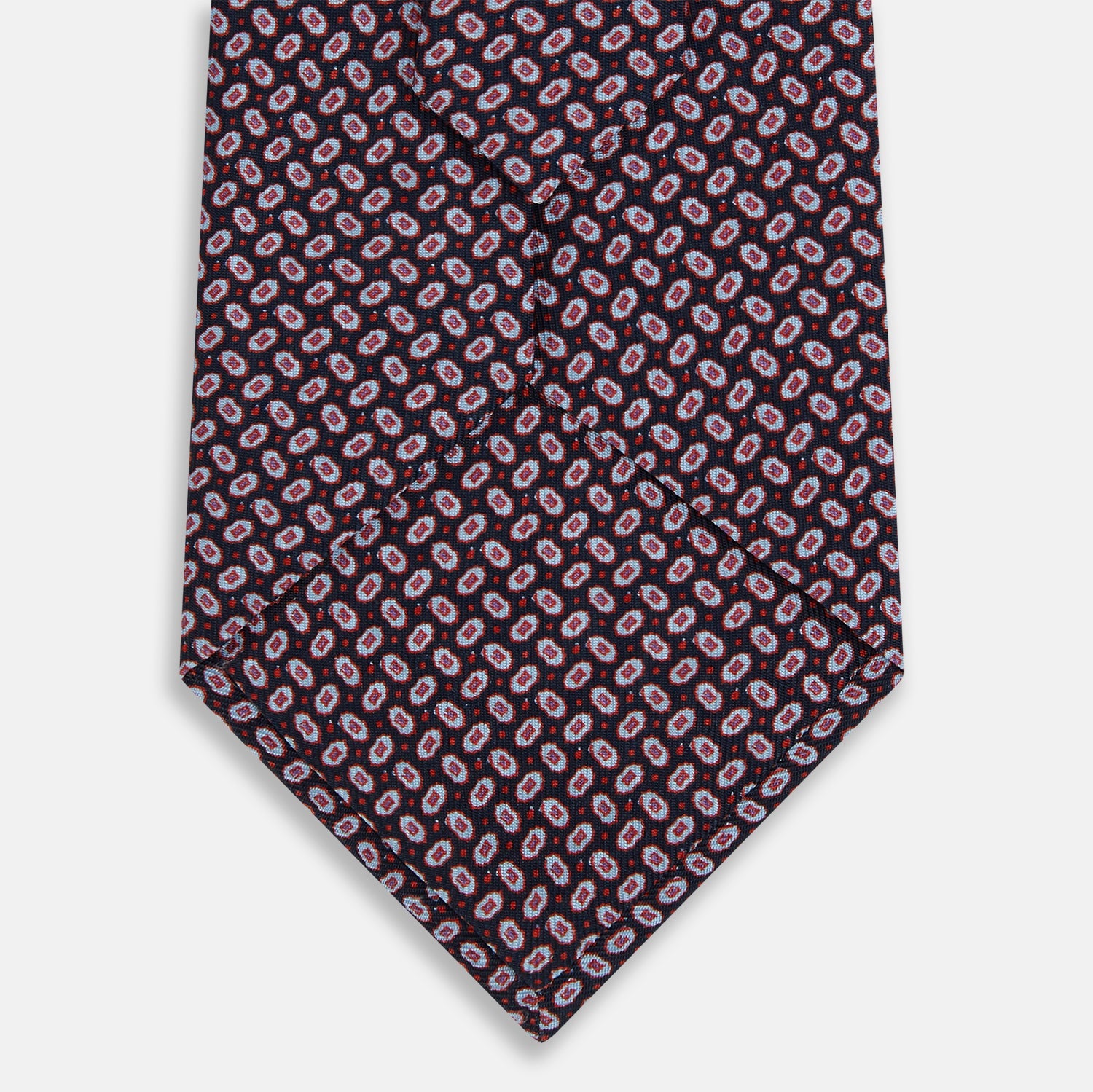 View 3 of product The Turnbull & Asser Red and Navy Oval-Patterned Silk Tie features a refined oval motif on navy silk, ideal for formal wear, and is showcased on a plain white background.