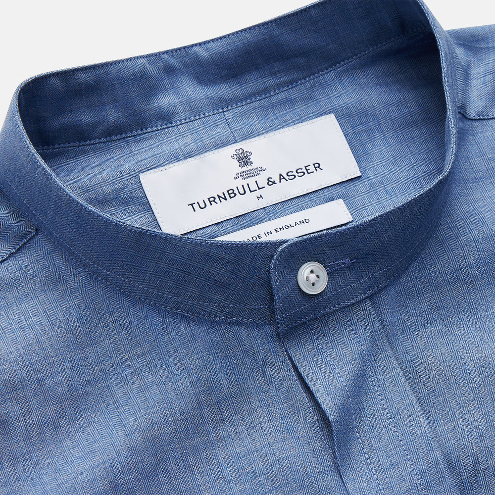 The Turnbull & Asser Blue Cotton Weekend Fit Blake Shirt features a light blue color, long sleeves, stand collar, white buttons, and a curved hem—ideal for casual weekends. Laid flat on a white background.