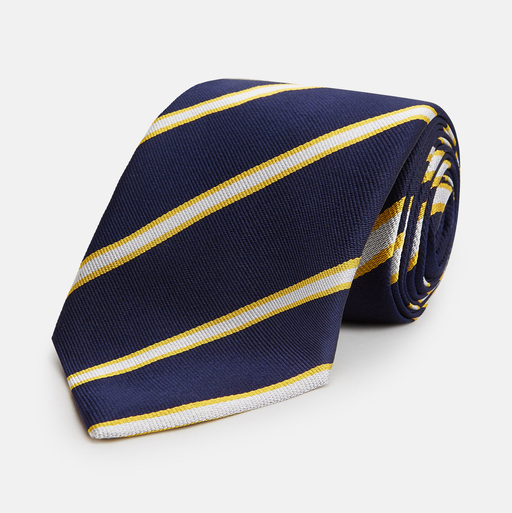 The Yellow and White Blazer Silk Tie by Turnbull & Asser, featuring diagonal white and yellow stripes on navy blue, is shown rolled up against a light gray background.