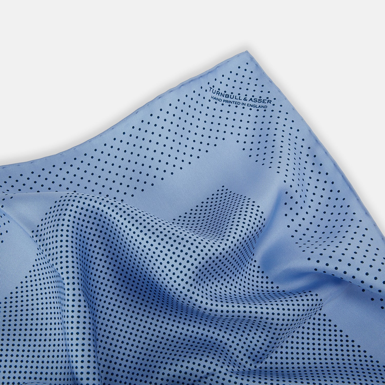View 2 of product The Turnbull & Asser Pale Blue Dot Silk Pocket Square features pure silk in pale blue with a border and scattered small navy polka dots, neatly folded with one corner turned down.