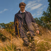 View 9 of product A man stands against a beige background, wearing the Turnbull & Asser Navy Burrows Double Breasted Coat over a plaid shirt and mauve cardigan, paired with dark rolled-up jeans and black shoes, looking directly at the camera with a neutral expression.