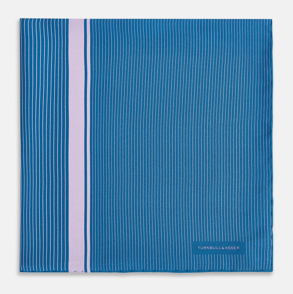 The Turnbull & Asser Blue and Lilac Stripe Silk Pocket Square features blue silk with white pinstripes, a bold lilac stripe near the edge, a turned-up corner revealing the reverse, and the brand name displayed in the bottom right.