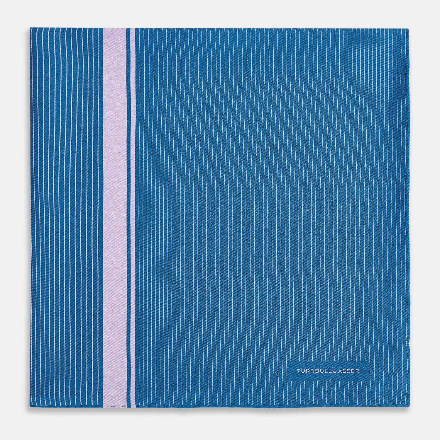 View 3 of product The Turnbull & Asser Blue and Lilac Stripe Silk Pocket Square features blue silk with white pinstripes, a bold lilac stripe near the edge, a turned-up corner revealing the reverse, and the brand name displayed in the bottom right.