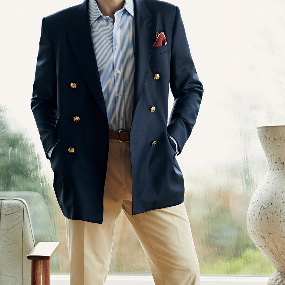 The Classic Navy Wool Blazer by Turnbull & Asser features a double-breasted design, gold buttons, notched lapels, and multiple front pockets, shown on a white background. This piece offers timeless, sophisticated nautical style.